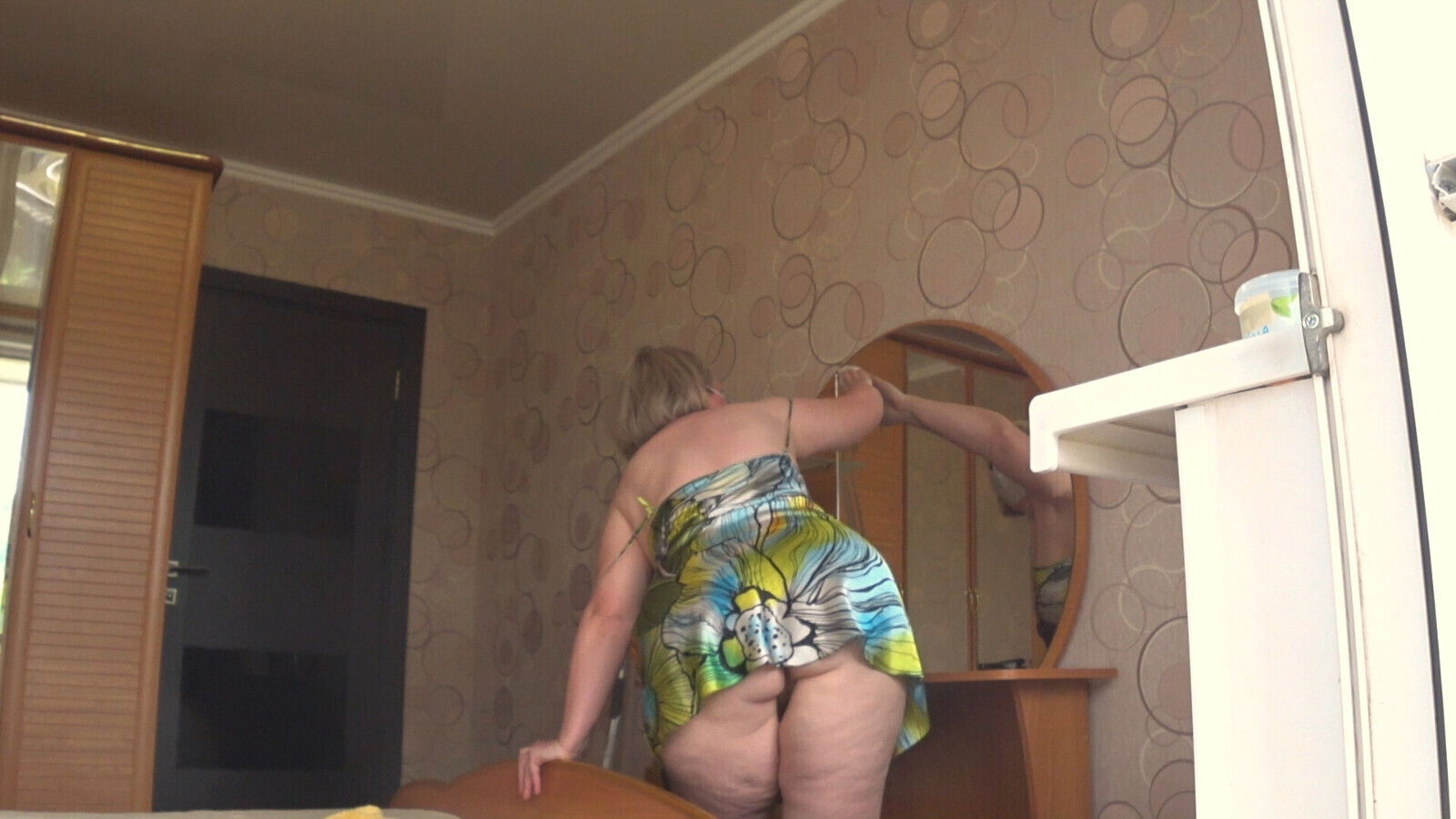 neighbor watches mature housewife through open window.