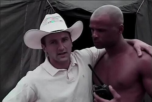 Playful white Paul Morgan lookng next salami smuggler narrative finds black volunteer Winston Love tented camp