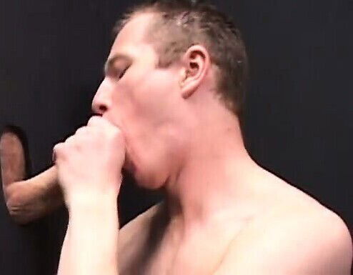 Cody Marsh kneeling before wall glory holes, slurping