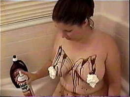 Busty Brunette pours chocolate sauce and whipped cream all over her tits in the tub